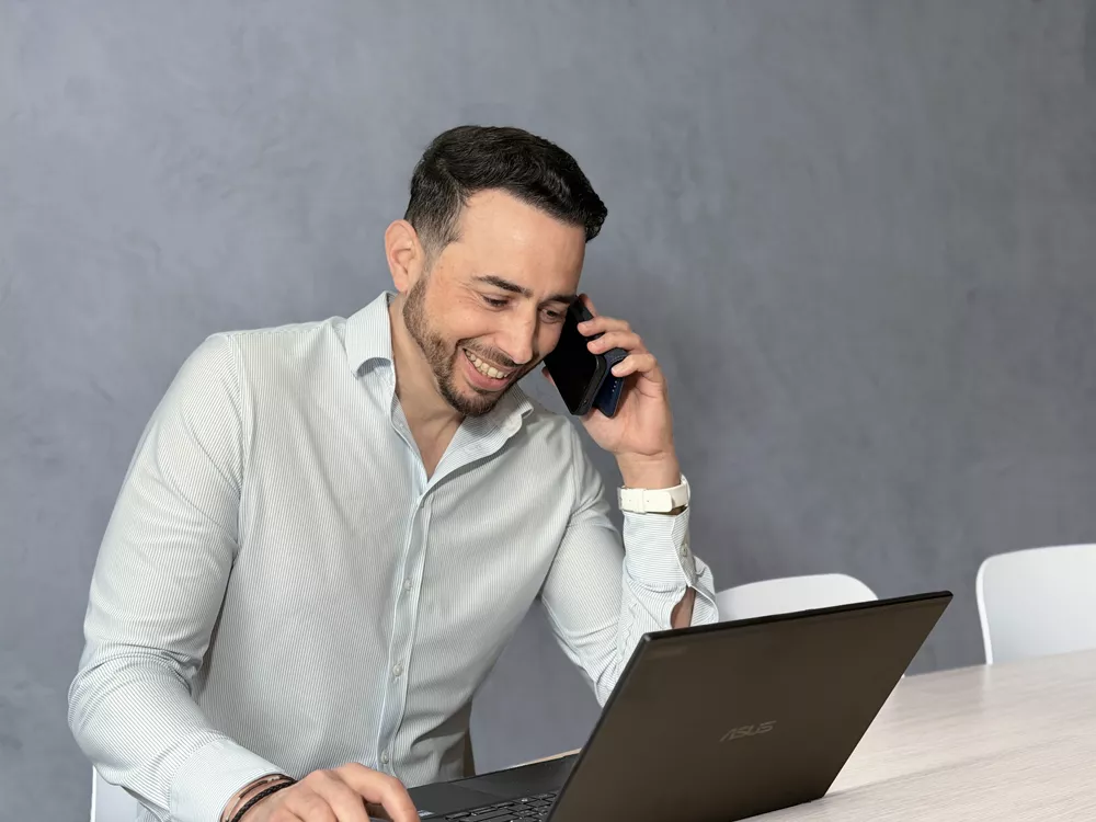 Homme souriant au téléphone devant un ordinateur portable